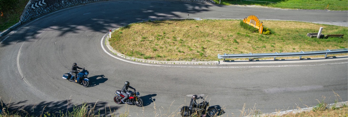 Three motorcycles are driving on a winding mountain road with guardrails and grassy areas.